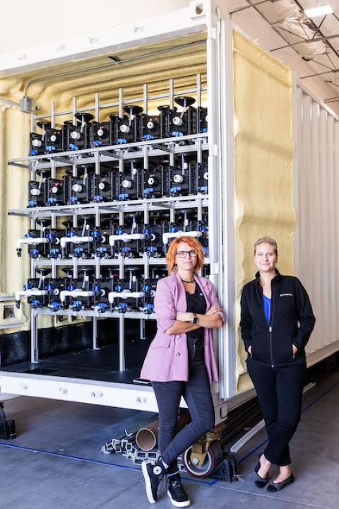 Orianna Bretschger and Sofia Babanova stand in front of a shipping container housing Aquacycl's BioElectrochemical Treatment Technology wastewater treatment system.