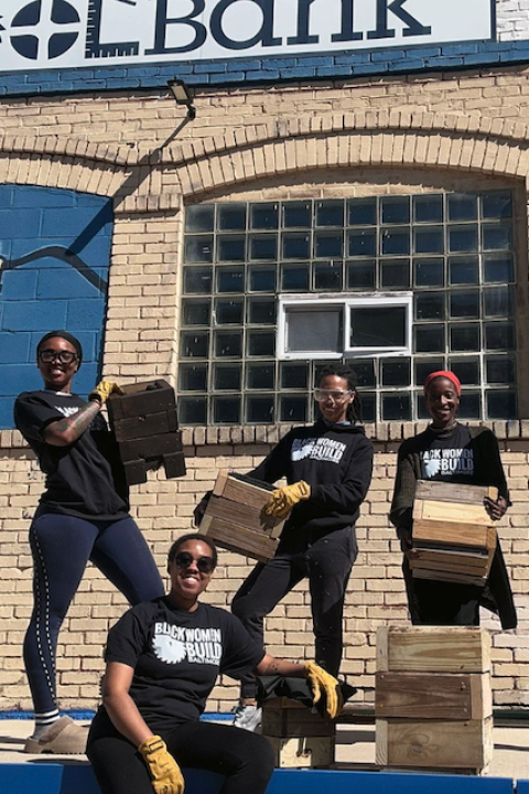 Several Black Women Build homeowners hold up planter boxes they made from recycled wood and smile at the camera.