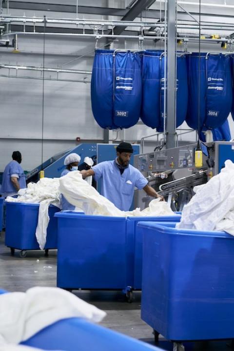 An employee separates white linens into large blue bins inside one of the Evergreen Laundry Cooperative facilities.