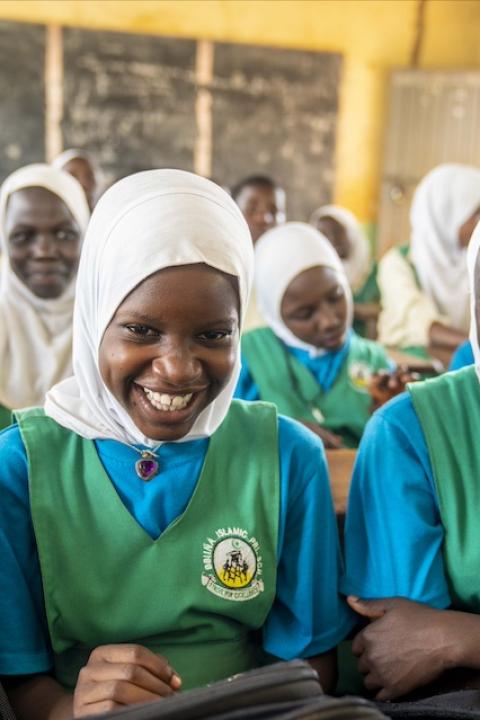 Two girls participating in Girls Up Initiative Uganda programming at their school smile at the camera.