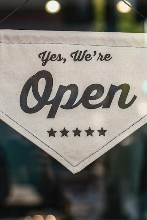 A sign on a window reads "yes, we're open" — social impact