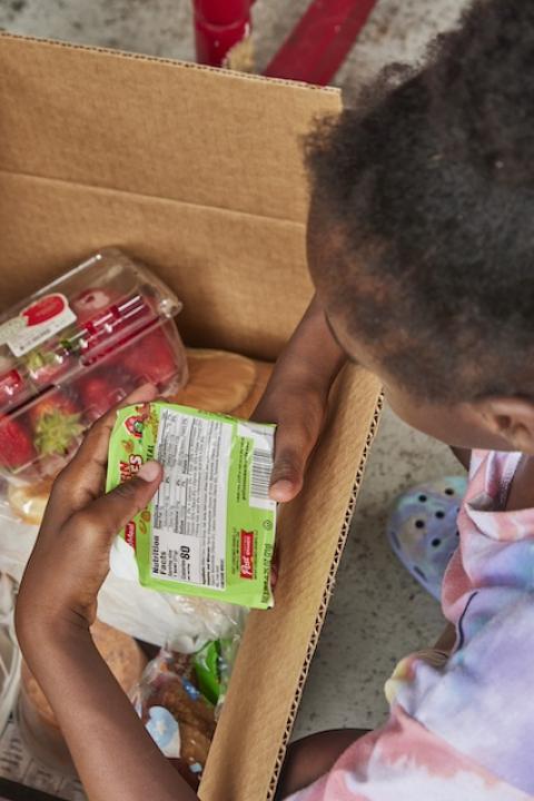 A child opens a box of food from the summer meal program. 