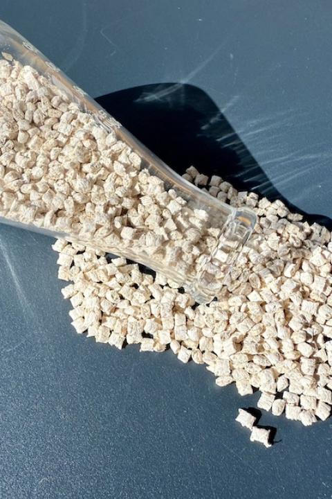 Small, white pieces of polypropylene grade plastic pouring out of a glass beaker — bioplastics