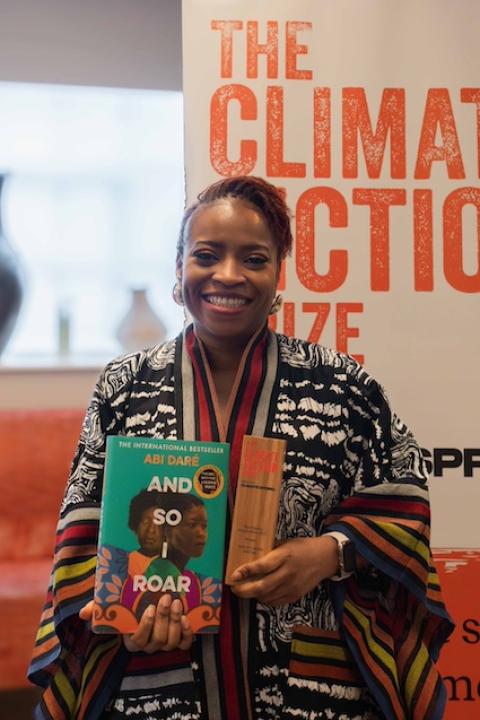 Abi Daré holds her winning novel, “And So I Roar," in one hand and the Climate Fiction Prize award in the other.