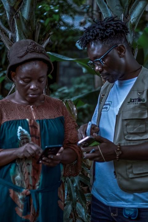 A Jambo Lab team member speaks with a woman, showing her how to use the platform on her mobile phone — early warning systems