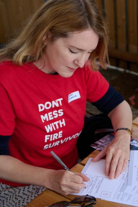 A person at an Extreme Weather Survivors event wears a "Don't mess with fire survivors" t-shirt while filling out a postcard to encourage leaders in California to take action after the LA wildfires.