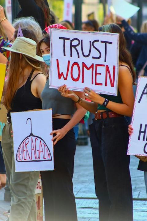 Protesters hold signs that read "Trust women" and "Abortion is health care" — maternal health