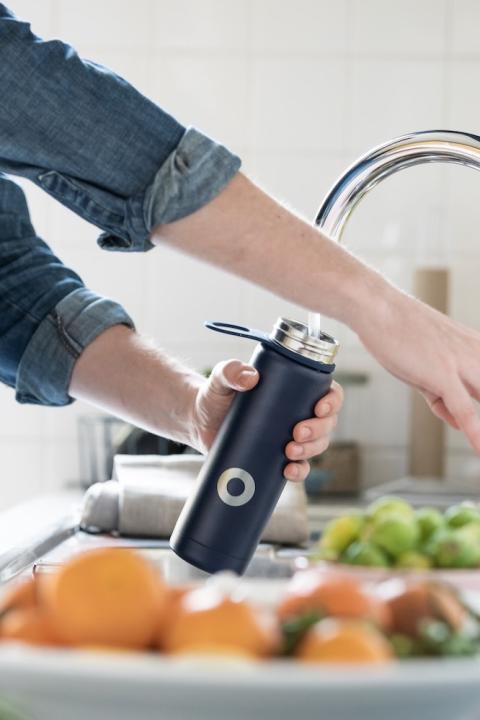 person filling up a reusable water bottle - sustainability behaviors