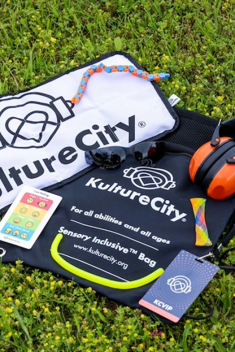 The contents of the KultureCity sensory inclusive bags, including fidget toys, strobe reduction glasses, a communication cue-card depicting emotions, and noise-reduction headphones — sensory inclusive events