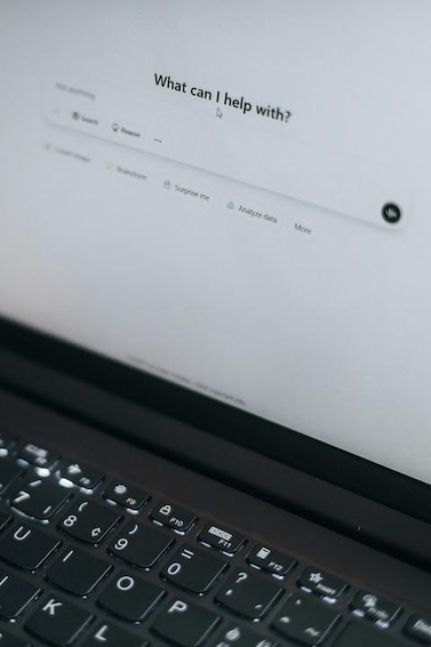 An open laptop displays the ChatGPT homepage, which reads, "What can I help with?" — AI