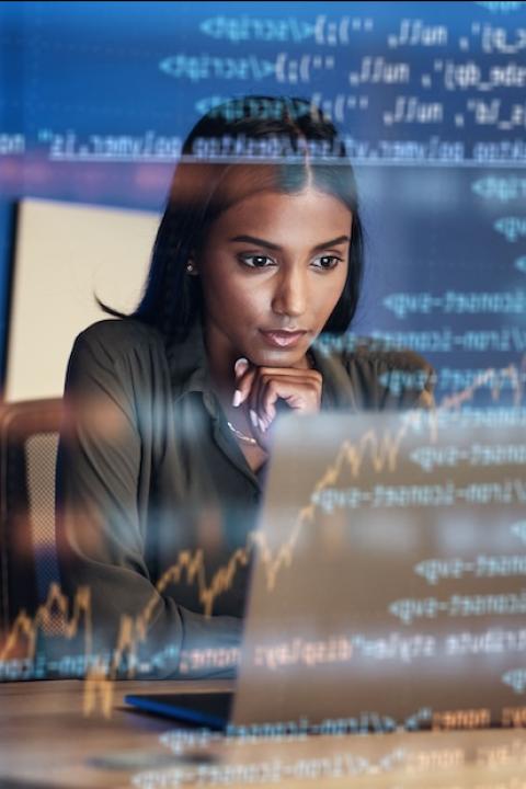 woman using the computer with hologram of code in front of her — women in tech
