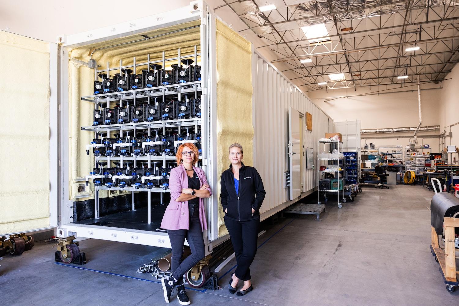 Orianna Bretschger and Sofia Babanova stand in front of a shipping container housing Aquacycl's BioElectrochemical Treatment Technology wastewater treatment system.