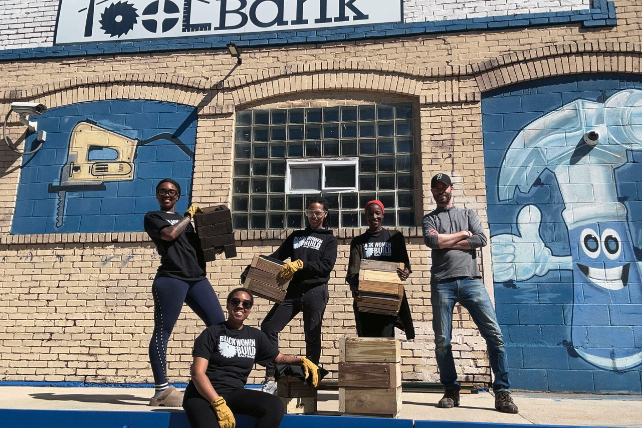 Several Black Women Build homeowners hold up planter boxes they made from recycled wood and smile at the camera.