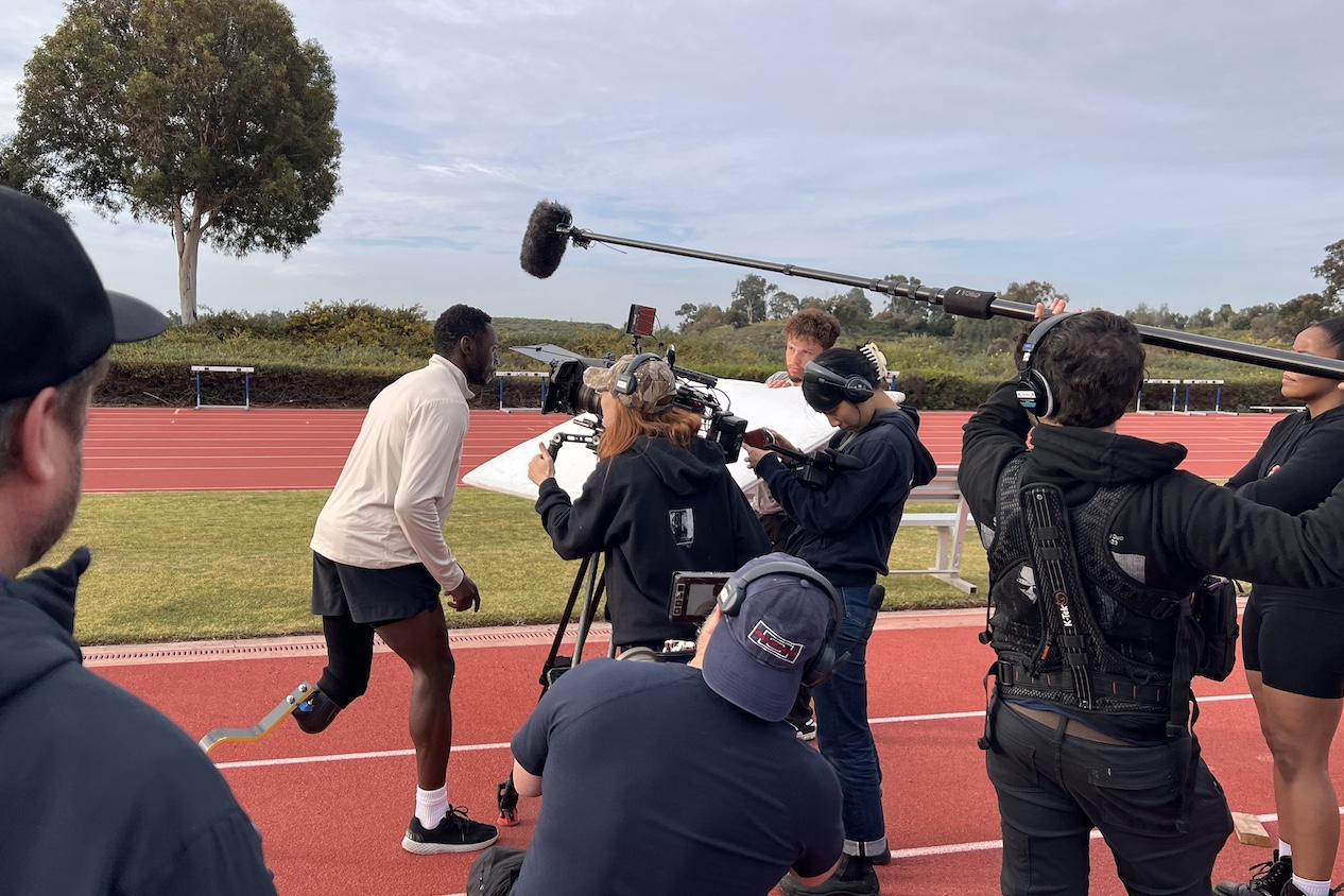 A crew films a public service announcement on a running track with Paralympic medalist Derek Loccident for the Creative Impact Lab.