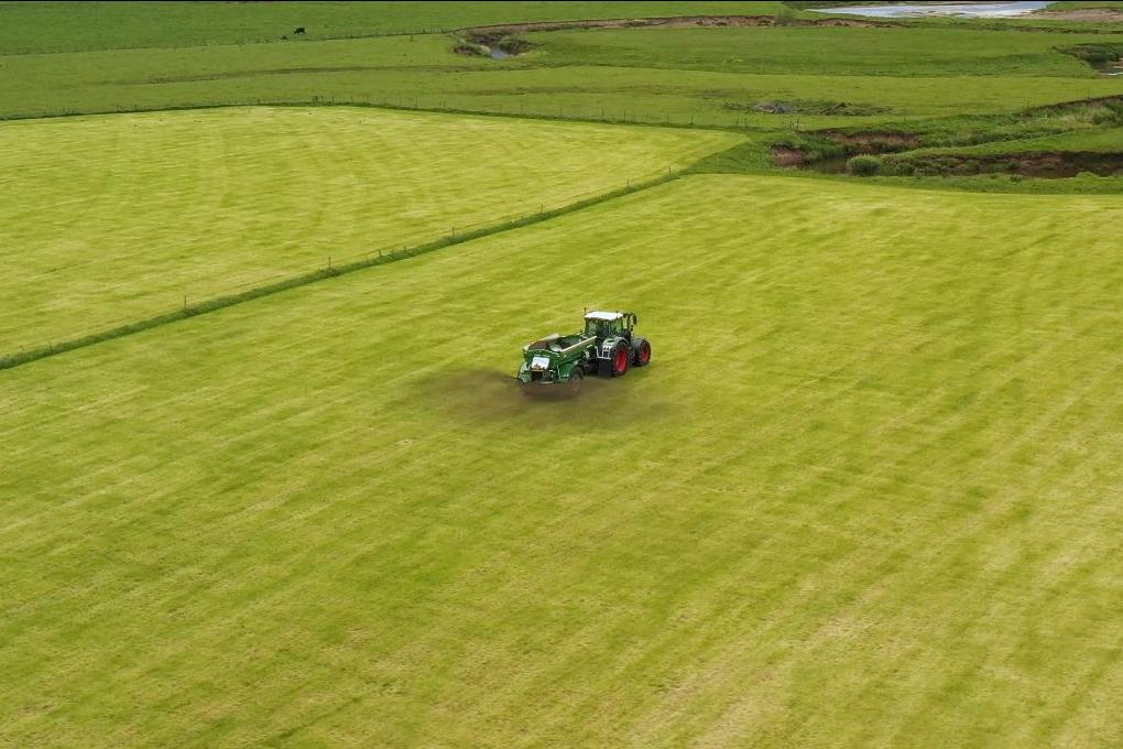 An aerial view of a tractor spreading crushed basalt rock on a farm field — enhanced rock weathering