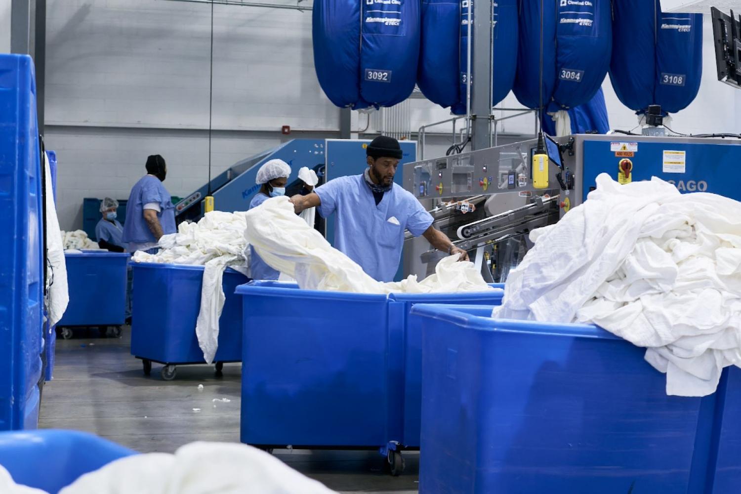 An employee separates white linens into large blue bins inside one of the Evergreen Laundry Cooperative facilities.