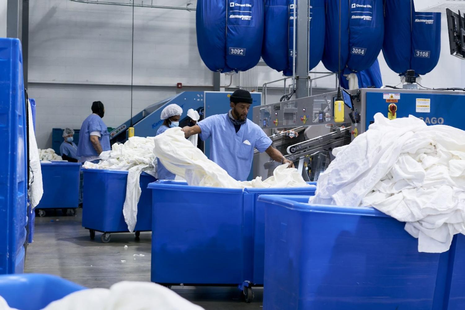 An employee separates white linens into large blue bins inside one of the Evergreen Laundry Cooperative facilities.