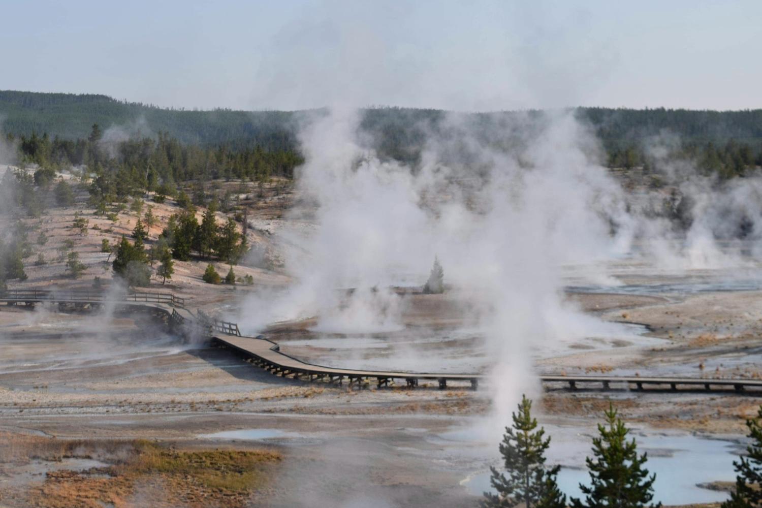 Steam rises up from a geyser basin, displaying of geothermal energy.