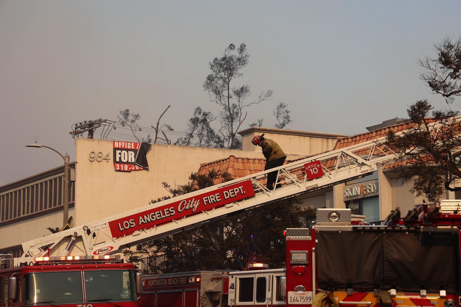 A firefighter climbs a fire truck ladder while responding to the Palisades Fire — LA wildfires