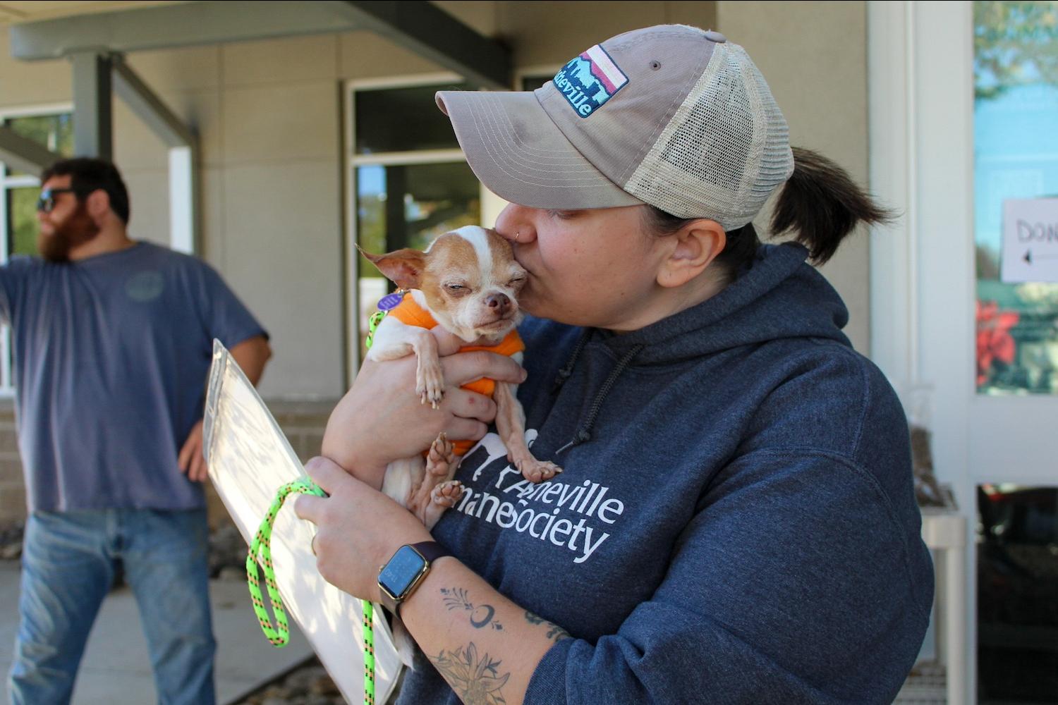 A member of the Asheville Humane Society kissing a small dog on the head during Hurricane Helene recovery efforts.
