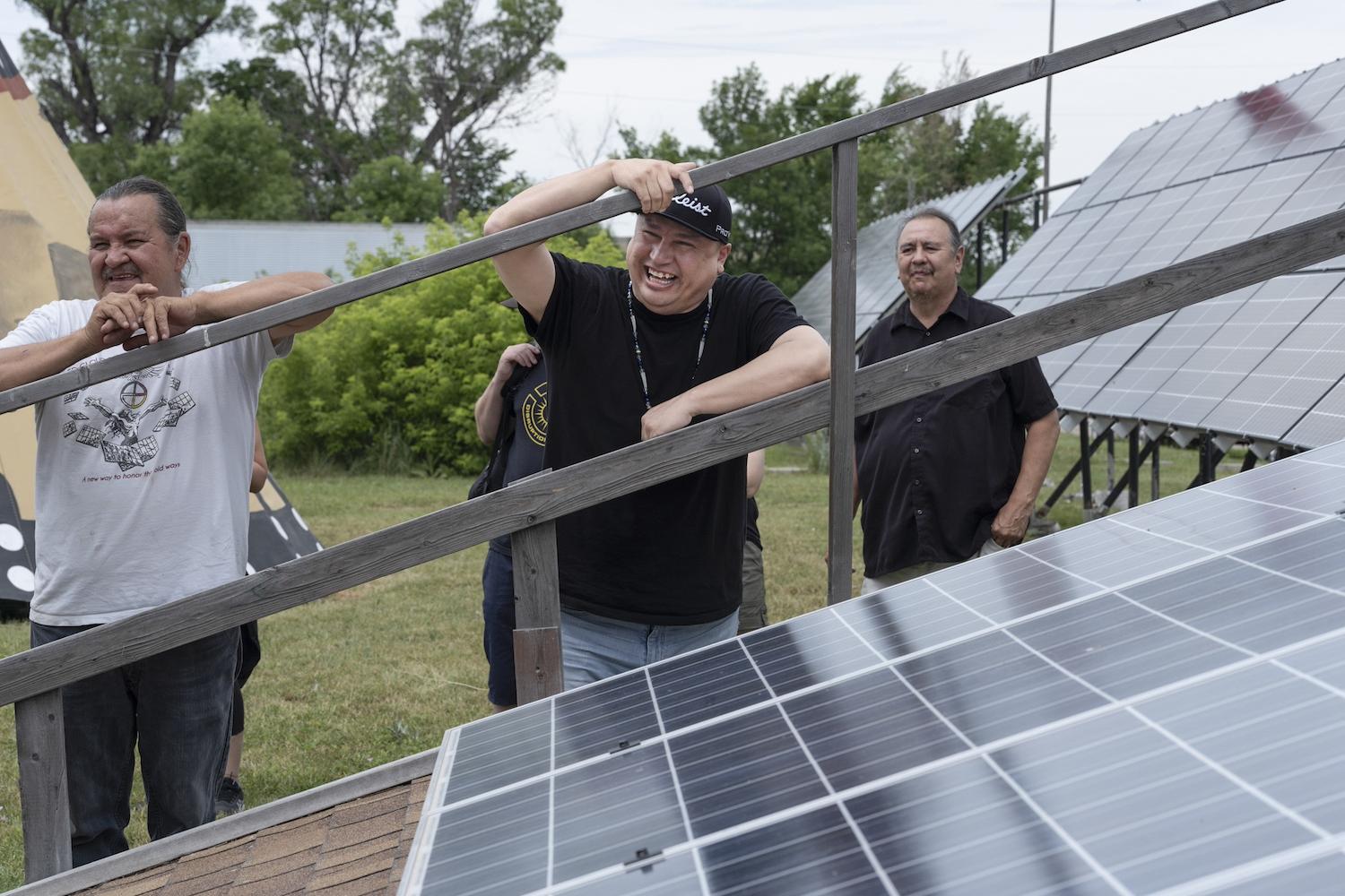 Cody Two Bears smiles while leaning on a solar panel array — energy sovereignty