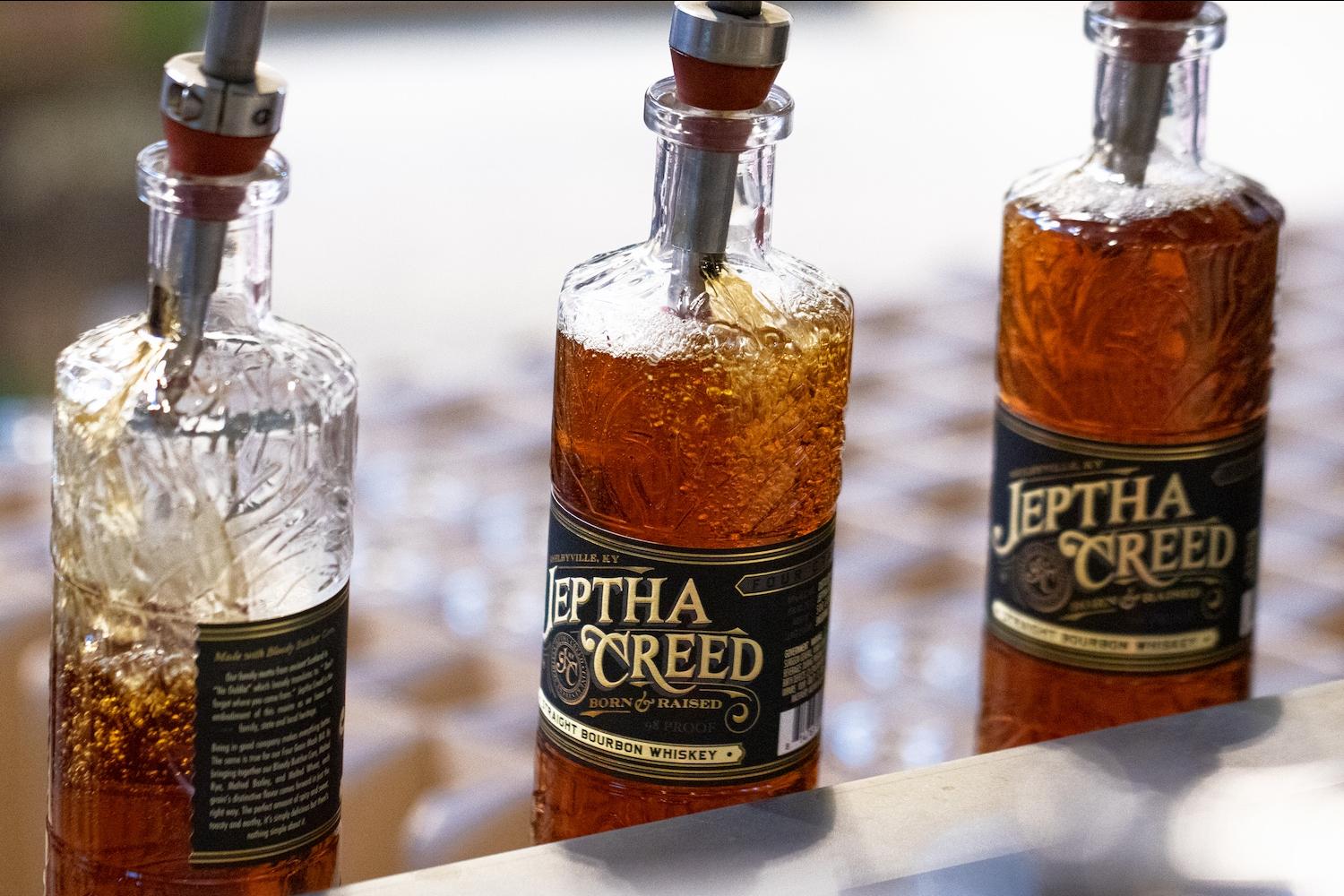 Bottles of Jeptha Creed bourbon being filled in an assembly line. 
