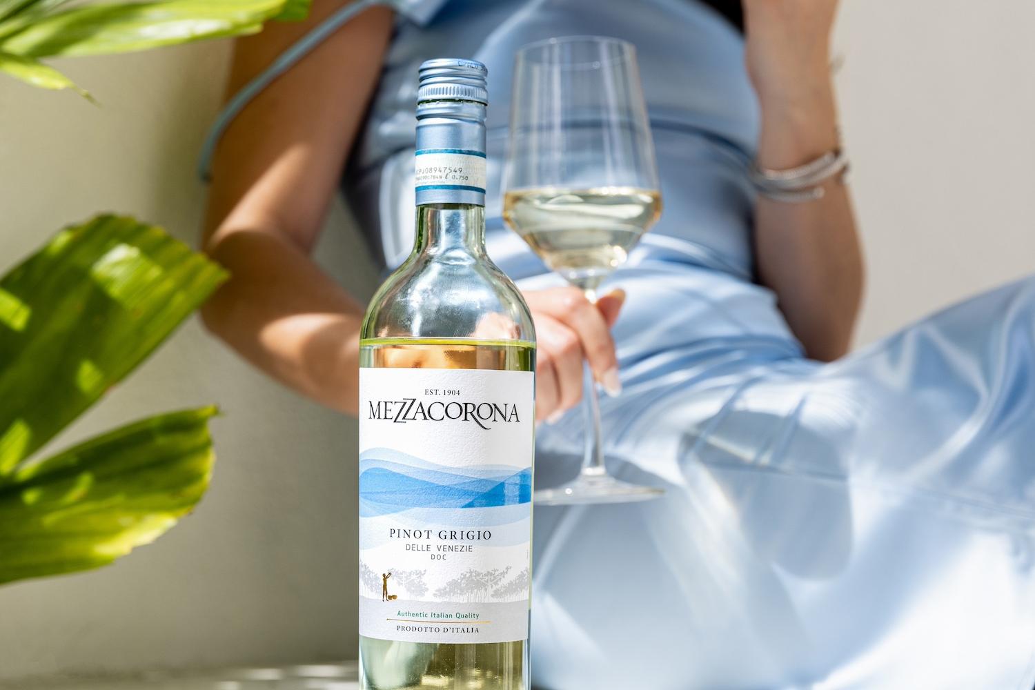 A woman sips Mezzacorona wine out of a glass while sitting next to the bottle — sustainable wine