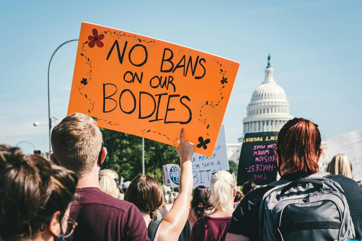 An attendee of a reproductive rights protest holds a sign that reads "No bands on our bodies."