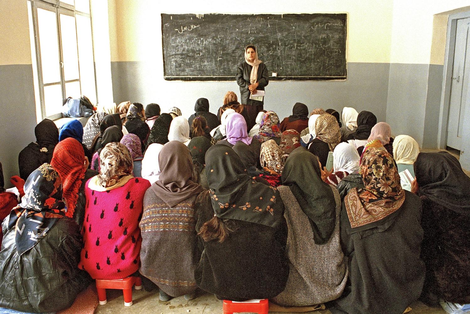 A class of young women sits in a school room in Afghanistan with a teacher at the front.