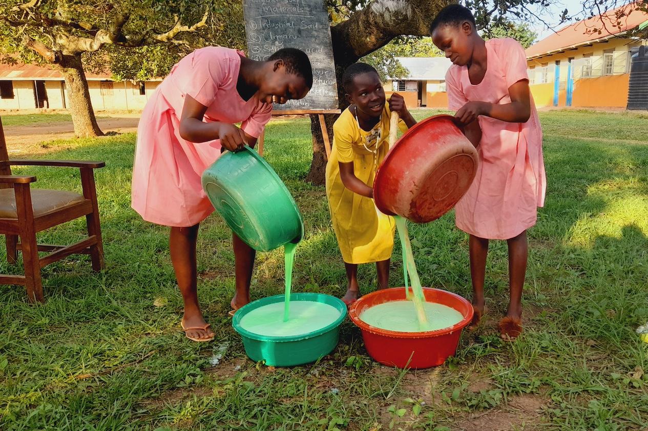 Three girls mix soap in buckets are a part of a Surge for Water soapmaking lesson.