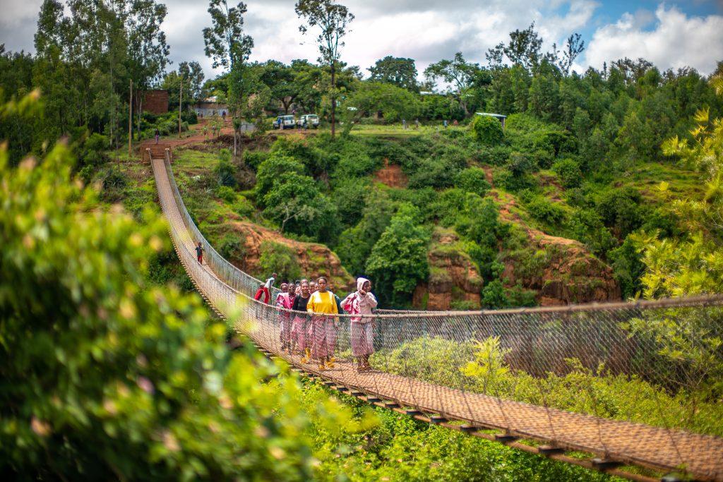 People walking across a bridge over a river valley in Africa — AI