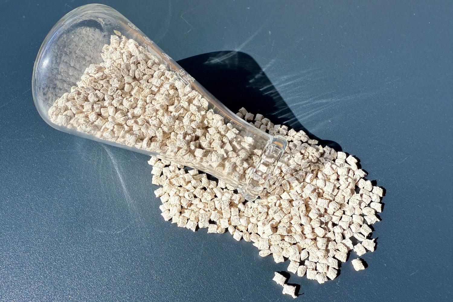Small, white pieces of polypropylene grade plastic pouring out of a glass beaker — bioplastics