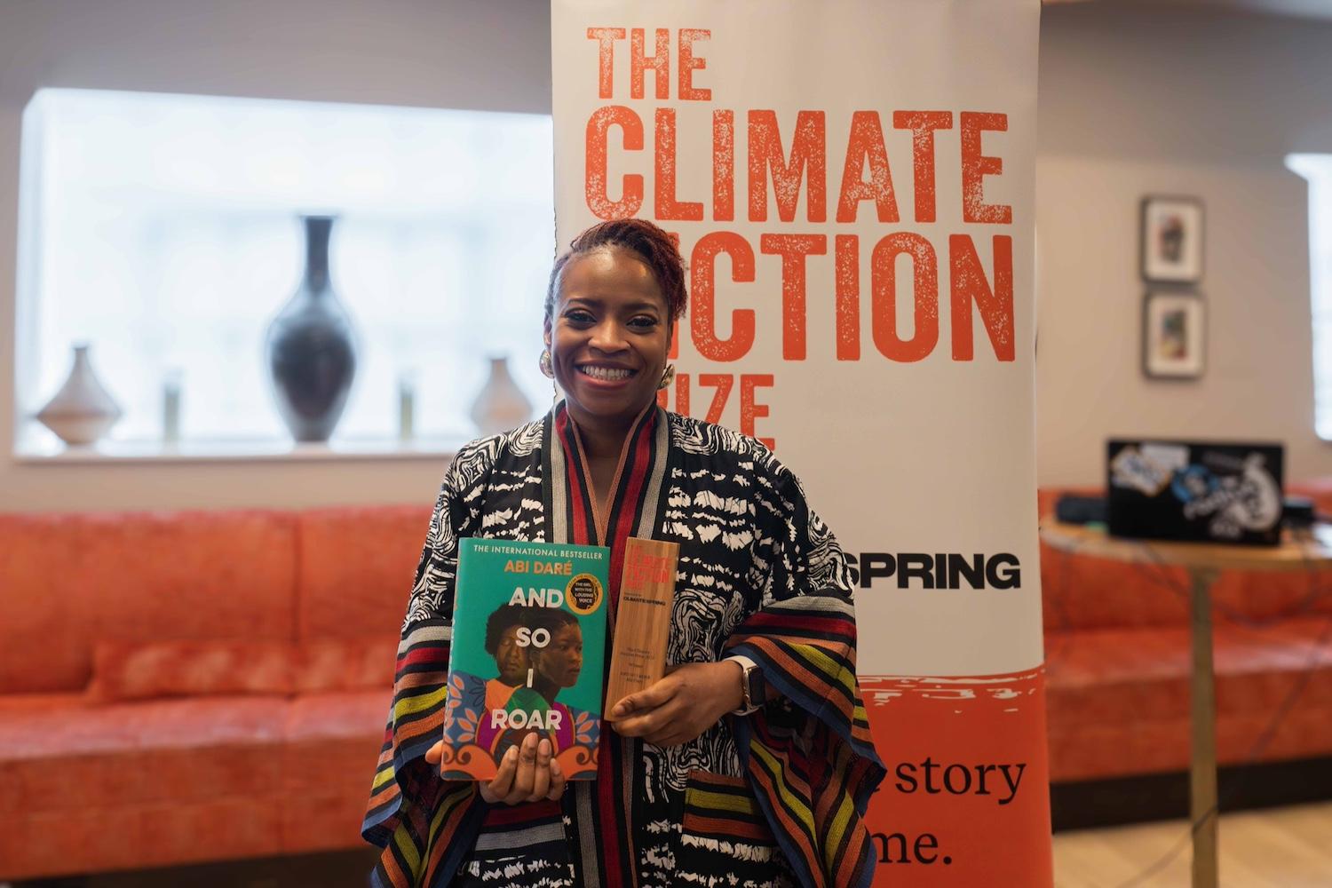 Abi Daré holds her winning novel, “And So I Roar," in one hand and the Climate Fiction Prize award in the other.
