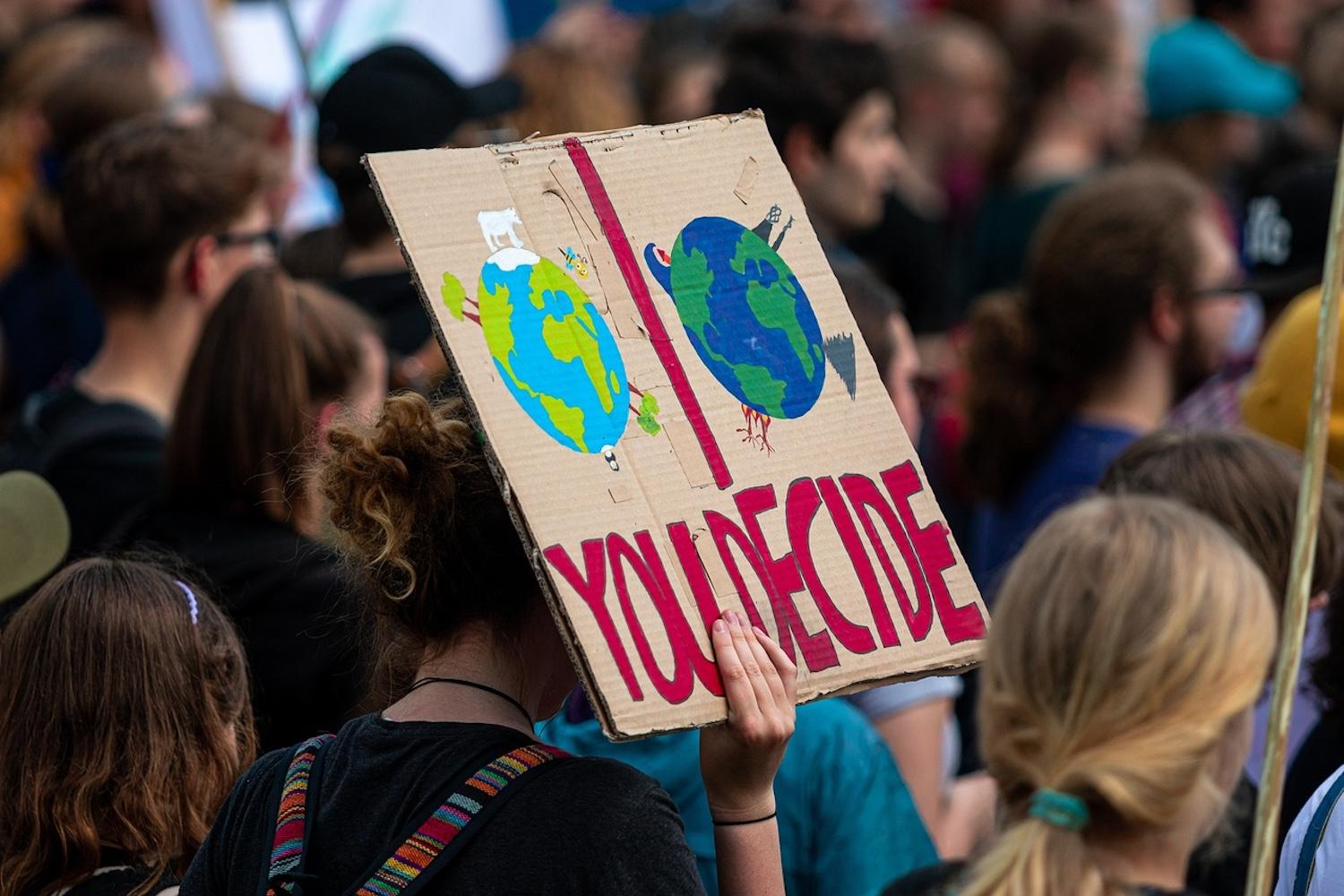 A climate activist holding a sign that reads, "You decide" — climate philanthropists
