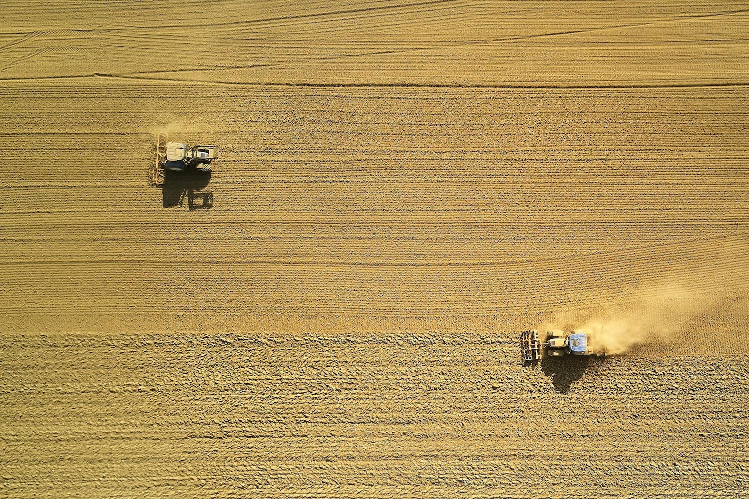An aerial view of two tractors harvesting a field — cover crops