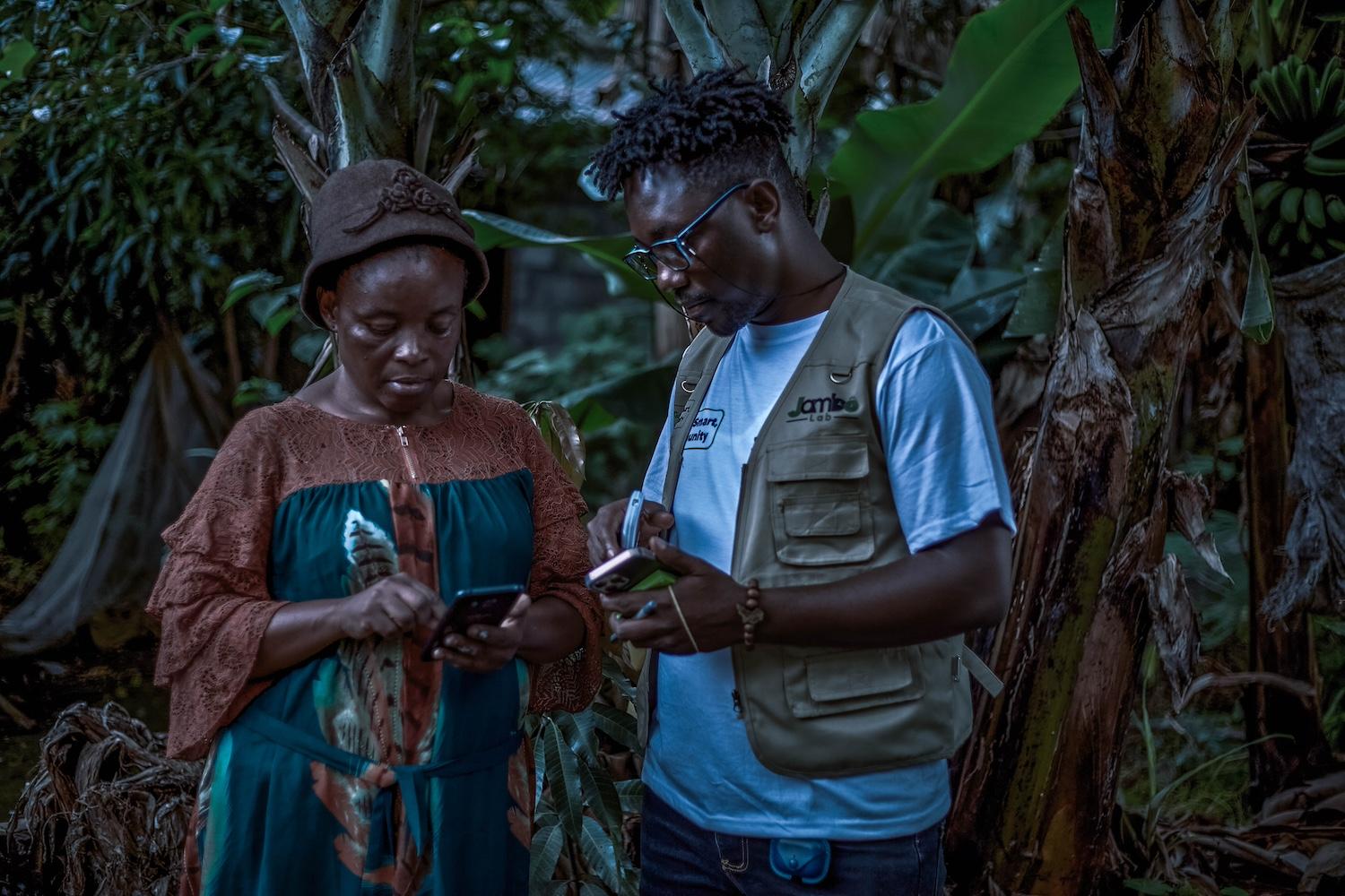 A Jambo Lab team member speaks with a woman, showing her how to use the platform on her mobile phone — early warning systems