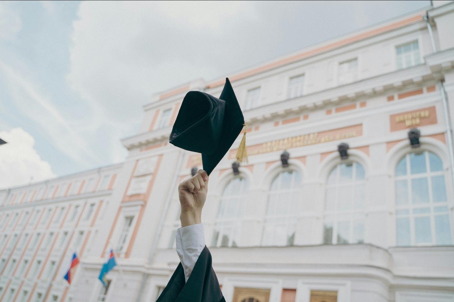 A person holding a graduation cap in the air — Excel Center