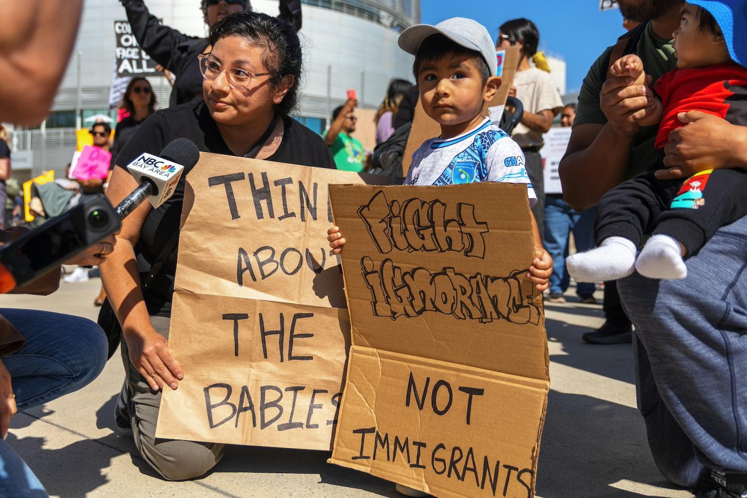A mother and child hold signs that read, "Think about the babies," and "Fight ignorance not immigrants," at a protest in California.