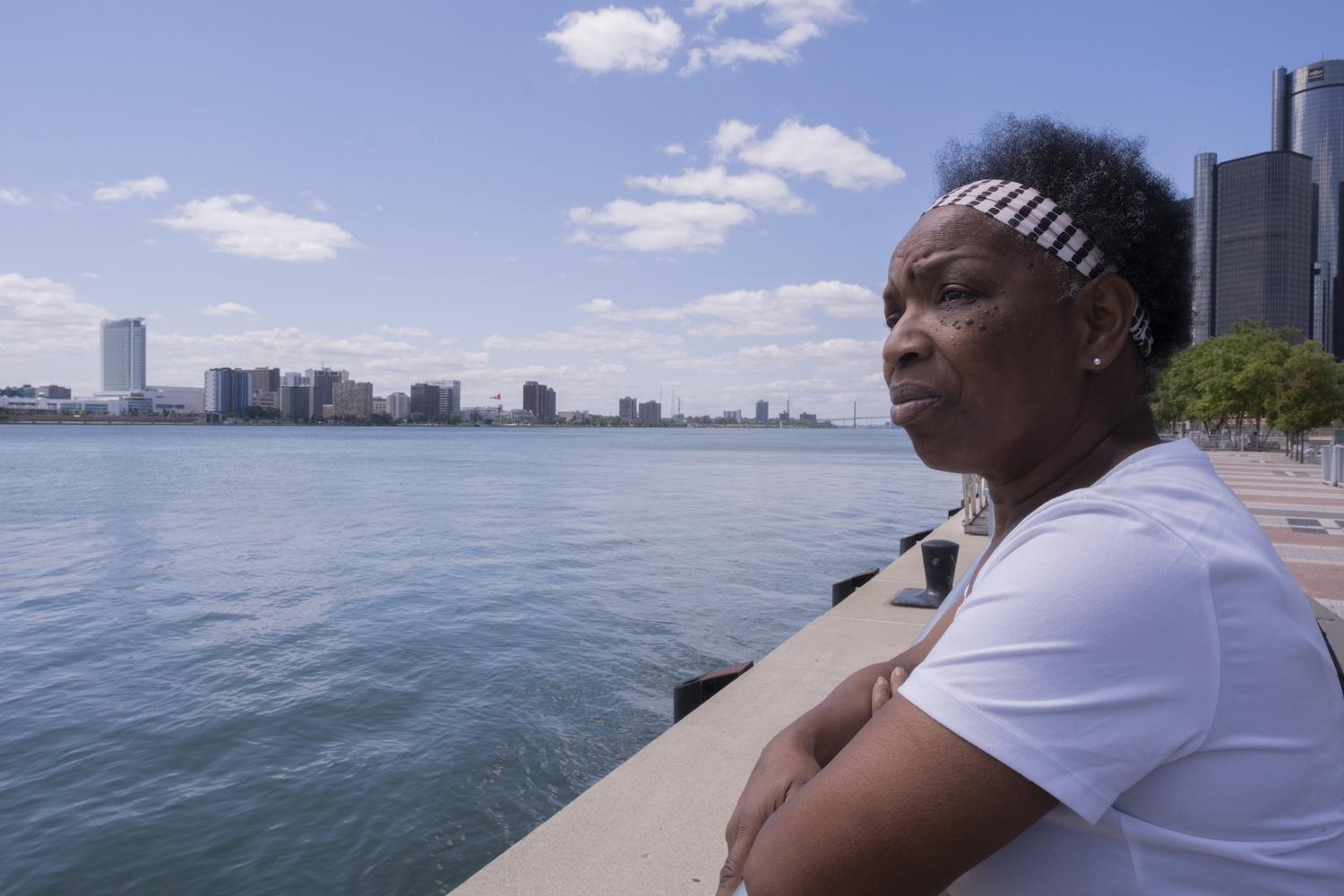 Sandra Turner-Handy overlooks a body of water with the Detroit skyline behind her — industrial air pollution