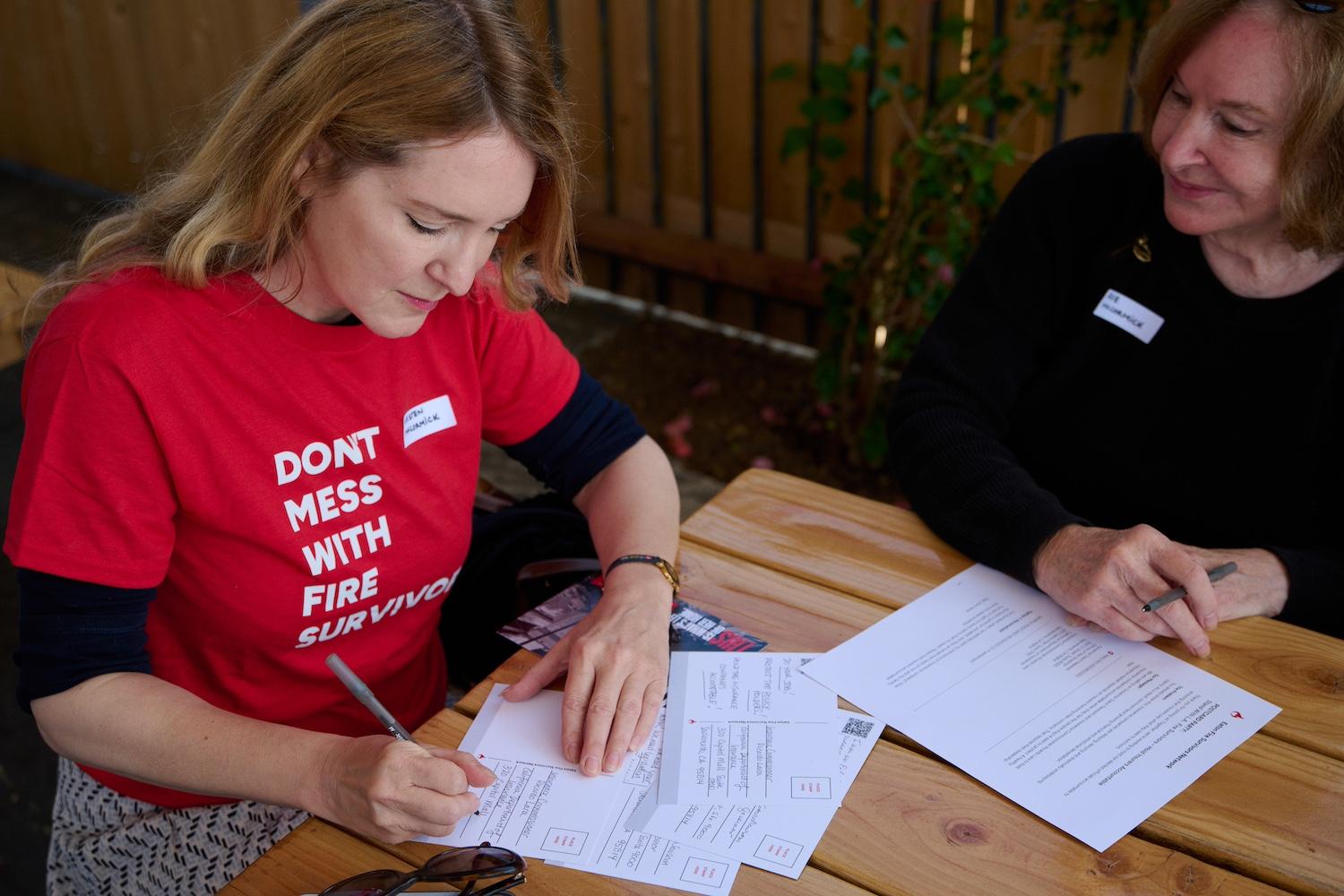 A person at an Extreme Weather Survivors event wears a "Don't mess with fire survivors" t-shirt while filling out a postcard to encourage leaders in California to take action after the LA wildfires.