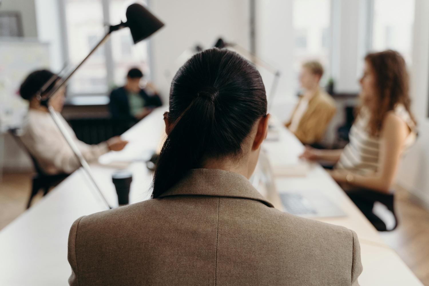 A woman sits at a table during a meeting with her back to the camera — menopause support