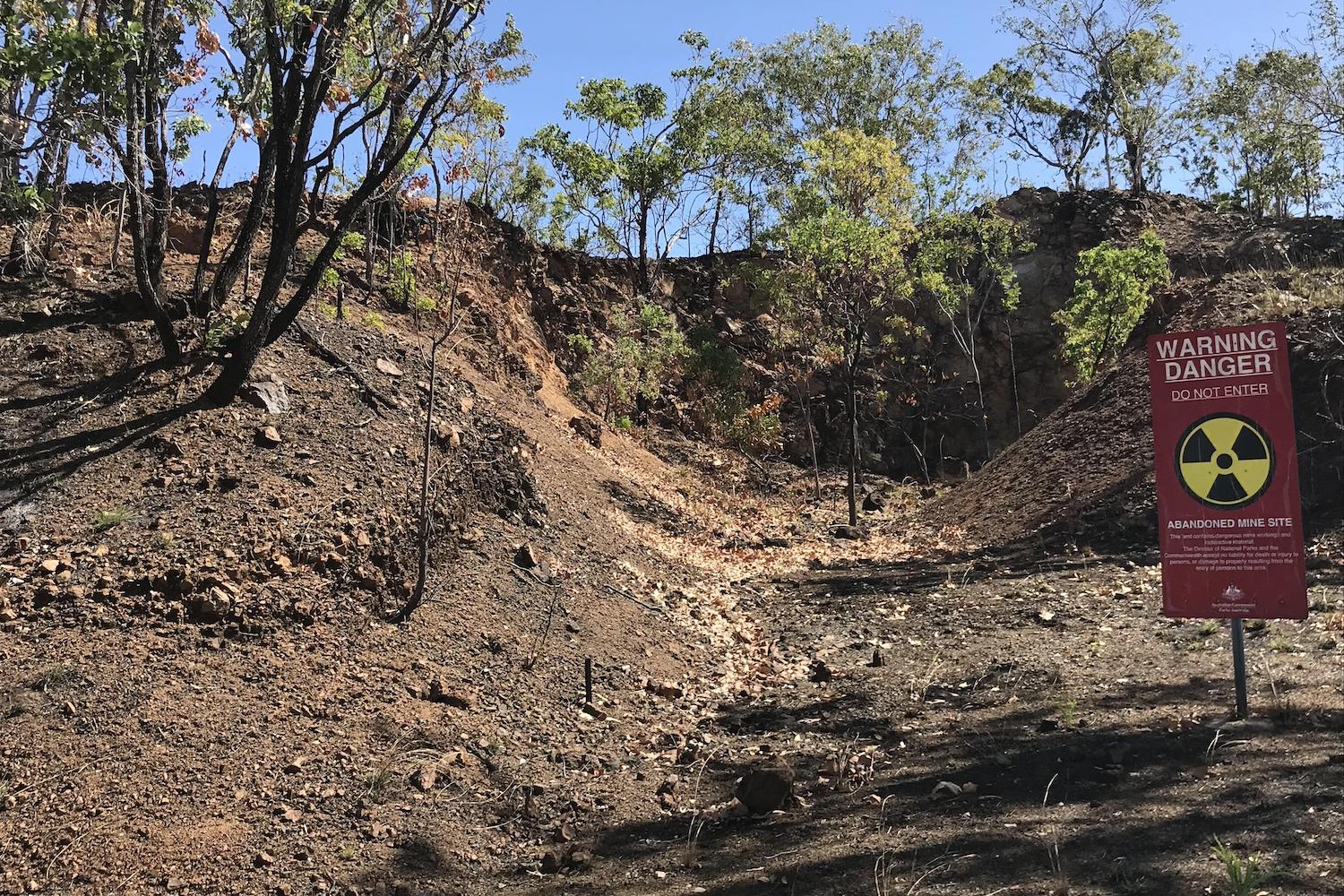 A danger warning sign sits in front of a mount of dirt a trees, designating an abandoned mining site in Australia.