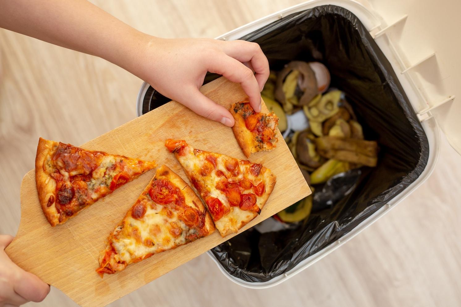 person discarding pizza and leftover food in the trash — reducing methane from food waste as a climate solution