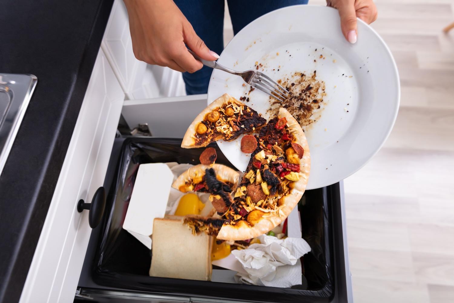 person throwing leftover pepperoni pizza in the trash - reducing food waste is one of the highest potential climate solutions globally