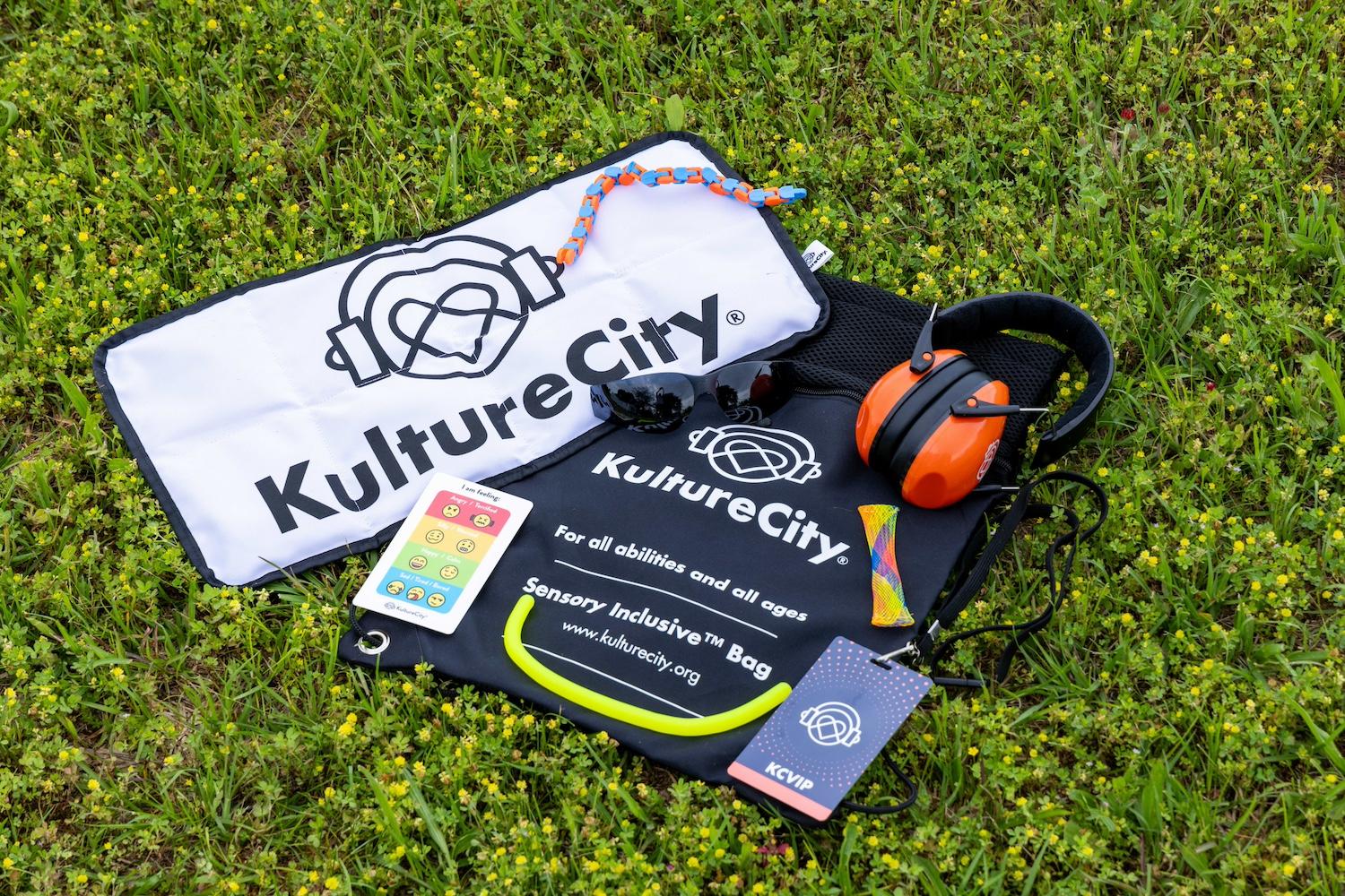 The contents of the KultureCity sensory inclusive bags, including fidget toys, strobe reduction glasses, a communication cue-card depicting emotions, and noise-reduction headphones — sensory inclusive events