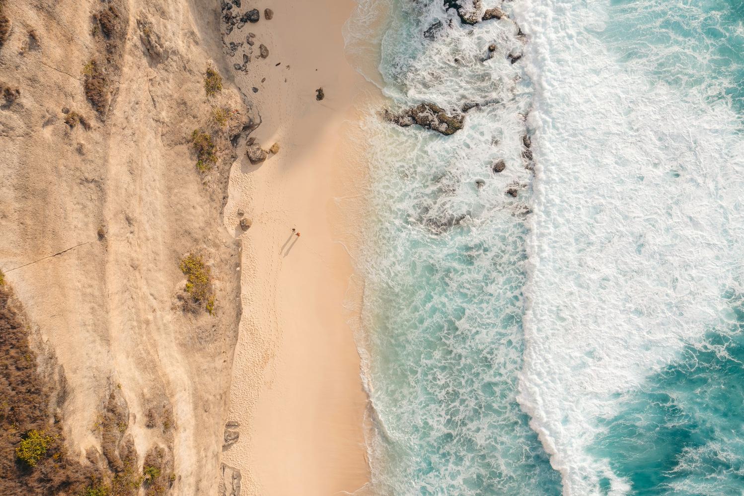 A birds eye view of two people walking along the beach — Sustainable Ocean Alliance