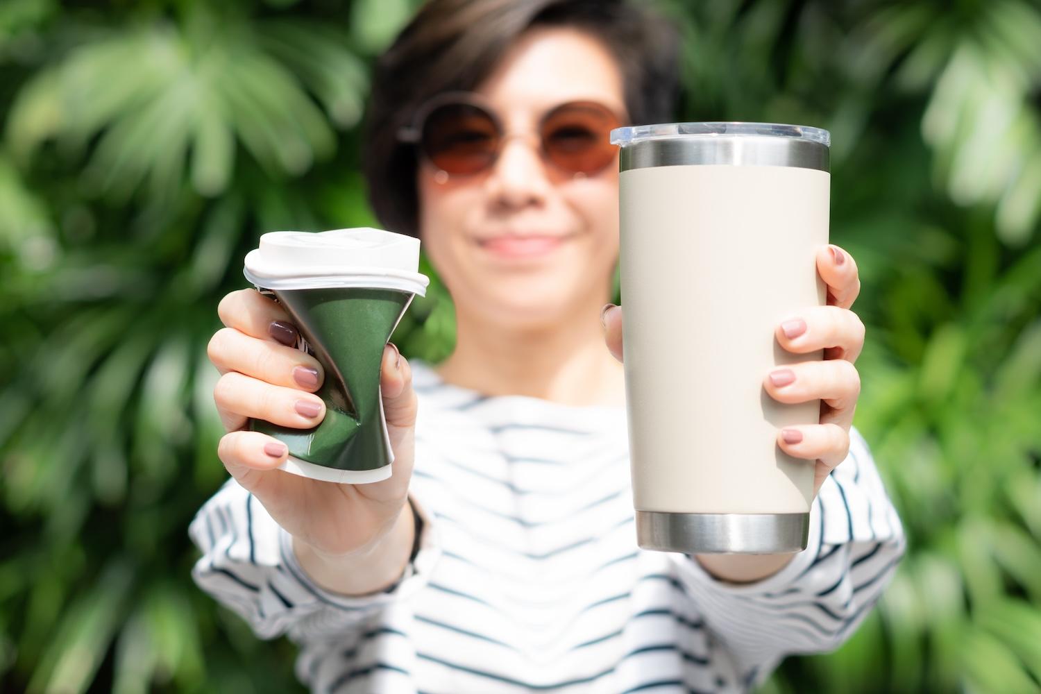 woman holding a single-use and reusable cup — how brands can help change consumer behavior