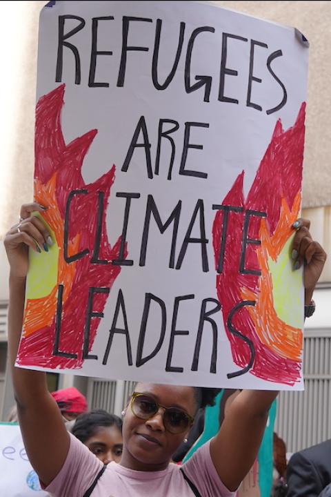 An activist holding a sign that reads "Refugees are climate leaders."