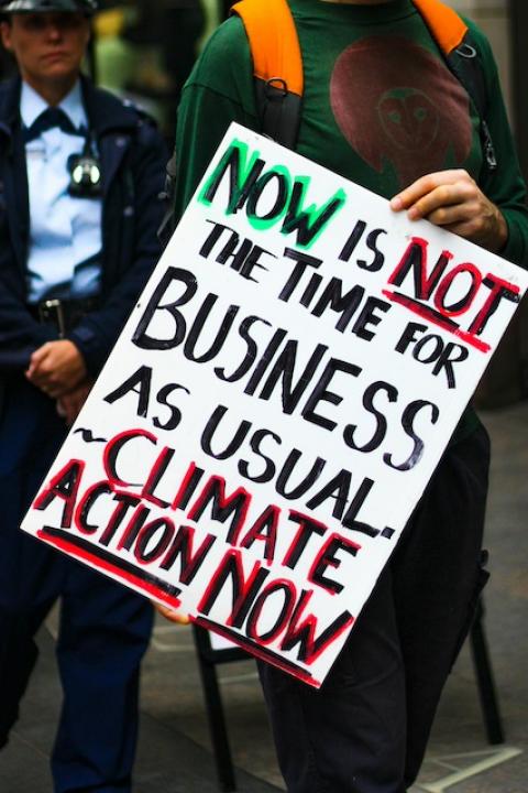 An activist with a sign that reads, "Now is not the time for business as usual. Climate action now." 
