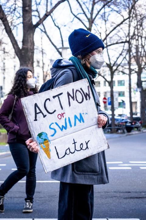 A climate activist holds a sign that states "act now or swim later." 